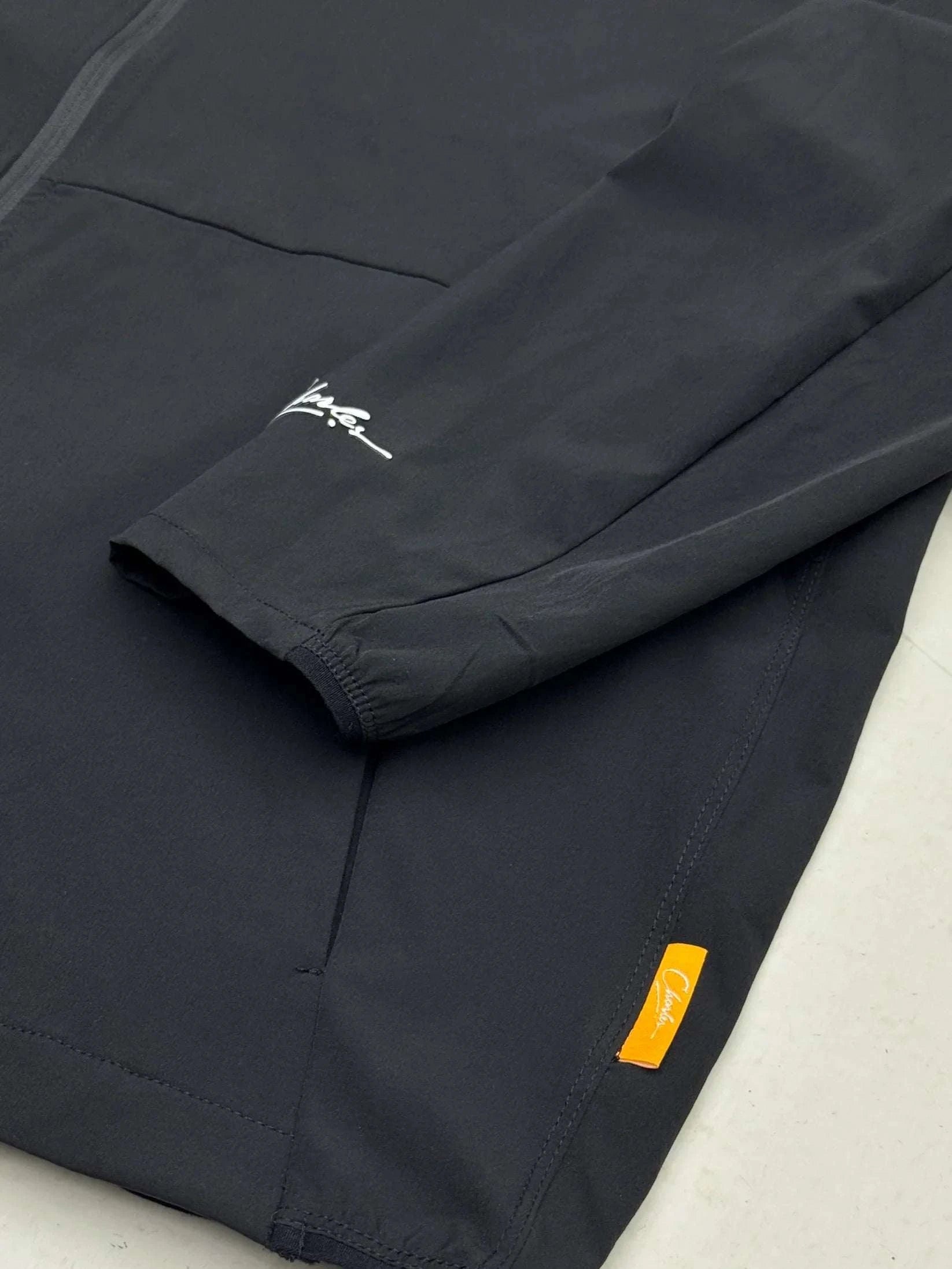 Close-up of Studio By Charles black track jacket sleeve and pocket with logo tags