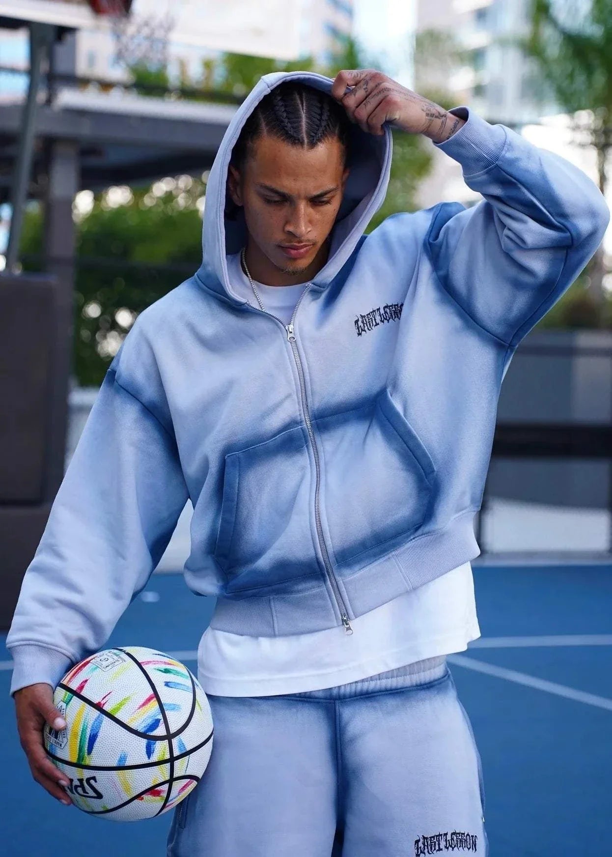 Last Lesson blue sprayed hoodie worn by a model holding a soccer ball.