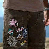 Last Lesson Badged Casazøna Shorts with colorful patches and logos on brown fabric