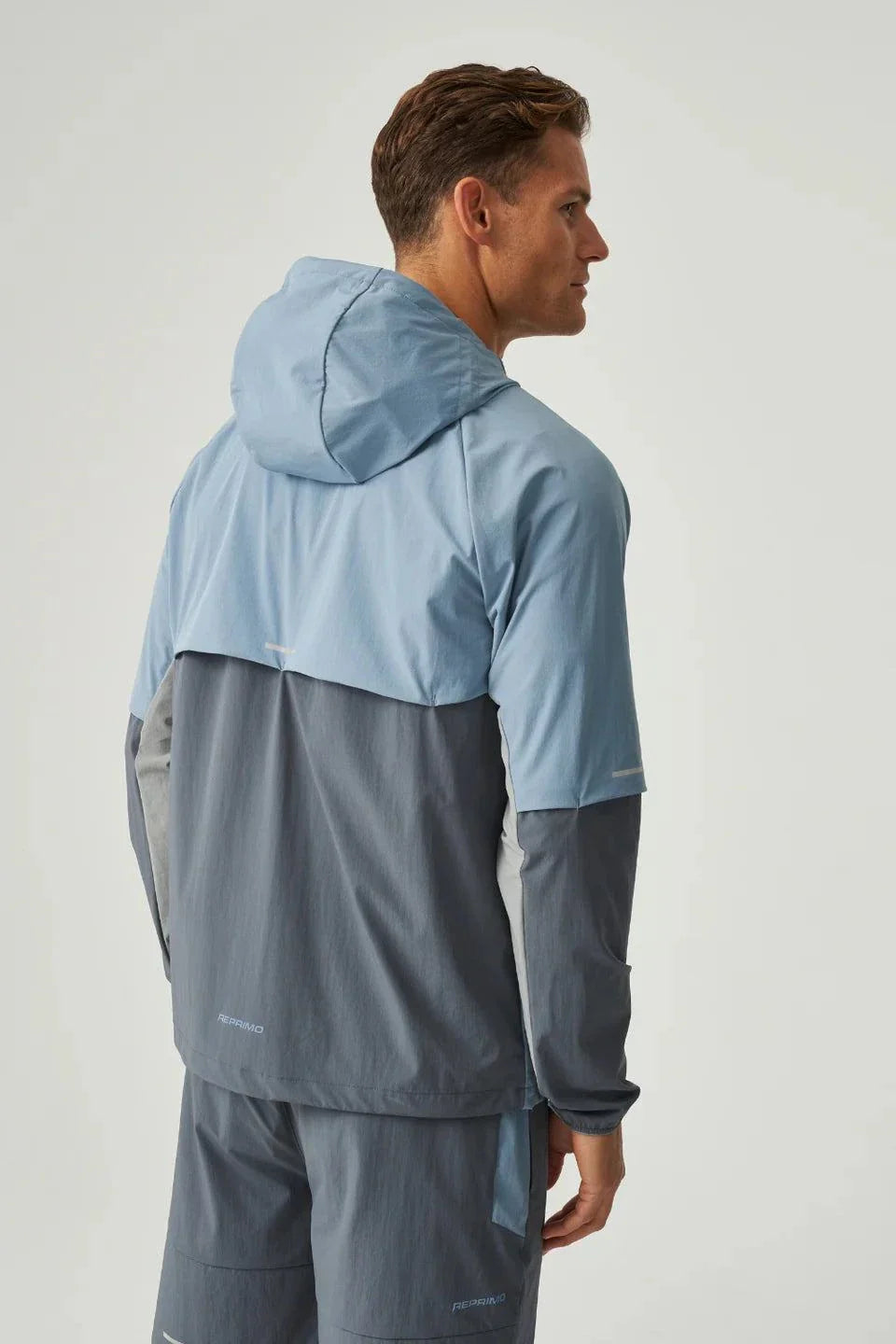 Man wearing dusky blue and turbulence Reprimo Vortex Windbreaker with ergonomic panels and reflective detailing viewed from the back