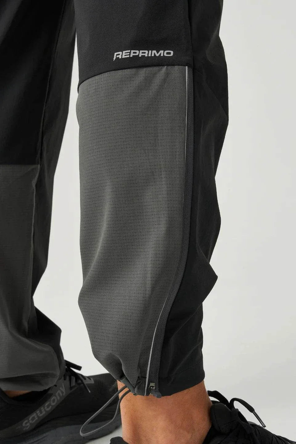 Close-up of Reprimo Clima Pants in black and charcoal showing breathable calf fabric and adjustable ankle cuffs for active performance.