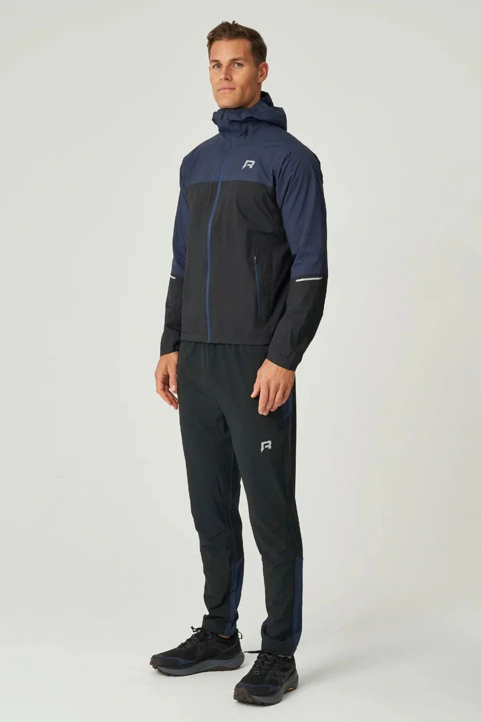 Male model wearing black and navy Reprimo Nova Pants with reflective strips and functional pockets for athletic performance and comfort