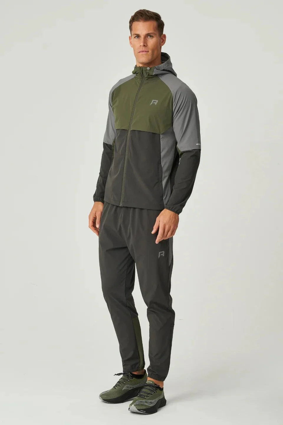 Man wearing olive and dark grey Reprimo Vortex Windbreaker with ergonomic design and reflective details