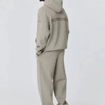 Man wearing grey Reprimo Collective Hoodie with matching pants and sneakers, showing back design and reflective logo.