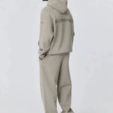 Man wearing grey Reprimo Collective Hoodie with matching pants and sneakers, showing back design and reflective logo.