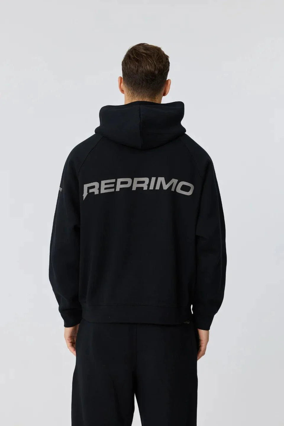Rear view of a man wearing black Reprimo Collective Hoodie with reflective logo and ergonomic fit
