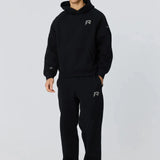 Man wearing black Reprimo Collective Hoodie and matching joggers with reflective logo, styled for athletic comfort and performance