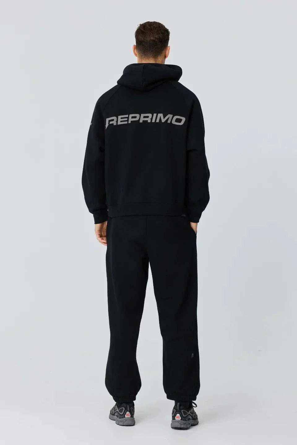 Back view of person wearing black Reprimo Collective Hoodie with reflective logo and ergonomic fit.