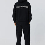 Back view of person wearing black Reprimo Collective Hoodie with reflective logo and ergonomic fit.