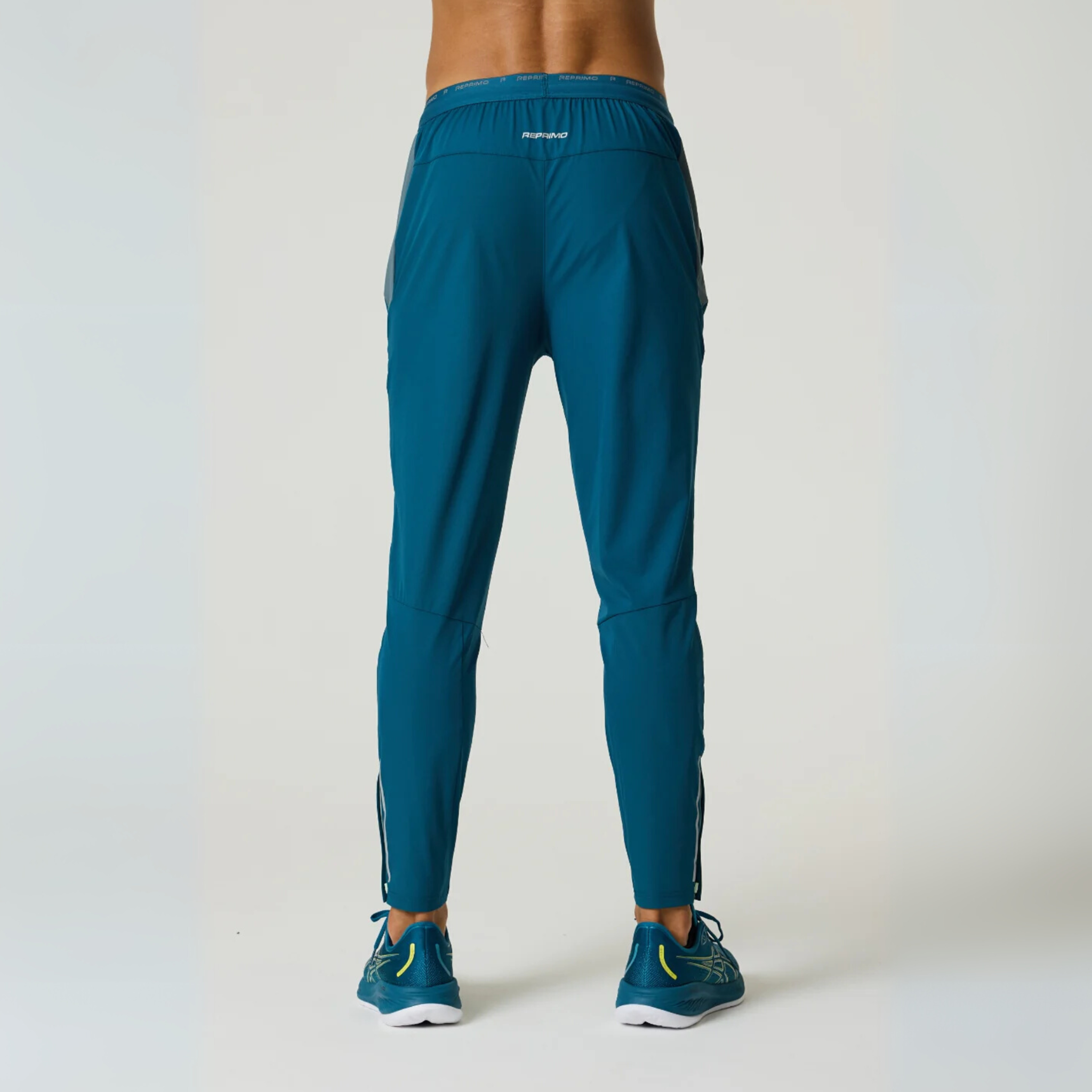 Back view of a person wearing Reprimo Flight Pants in tidal teal and blue steel, featuring a slim fit and elastic waistband.