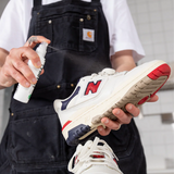 Person spraying SneakersER Clean & Protect solution on white and red New Balance sneaker