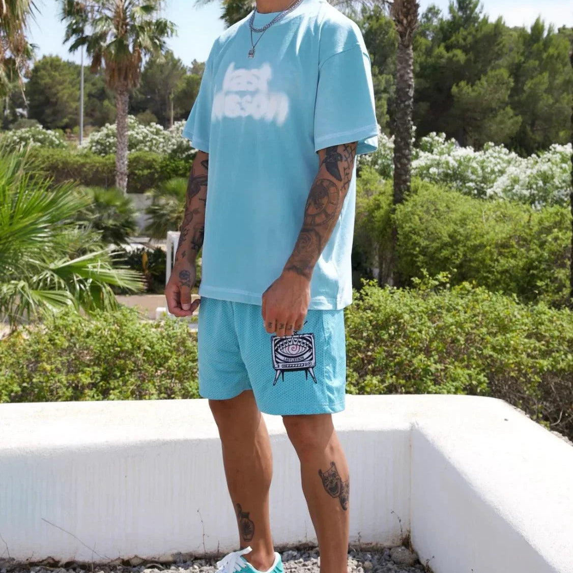 Man wearing Last Lesson Blue Blurred T-Shirt outdoors with palm trees.