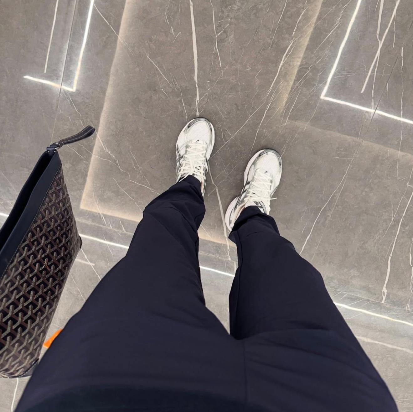 Person wearing Studio By Charles navy trackpants and white sneakers standing on a tiled floor next to a patterned bag