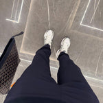 Person wearing Studio By Charles navy trackpants and white sneakers standing on a tiled floor next to a patterned bag
