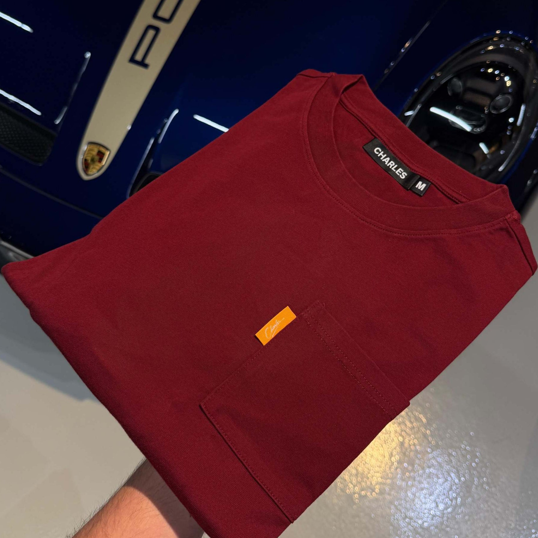 Studio By Charles burgundy long sleeve tee folded on blue Porsche car hood