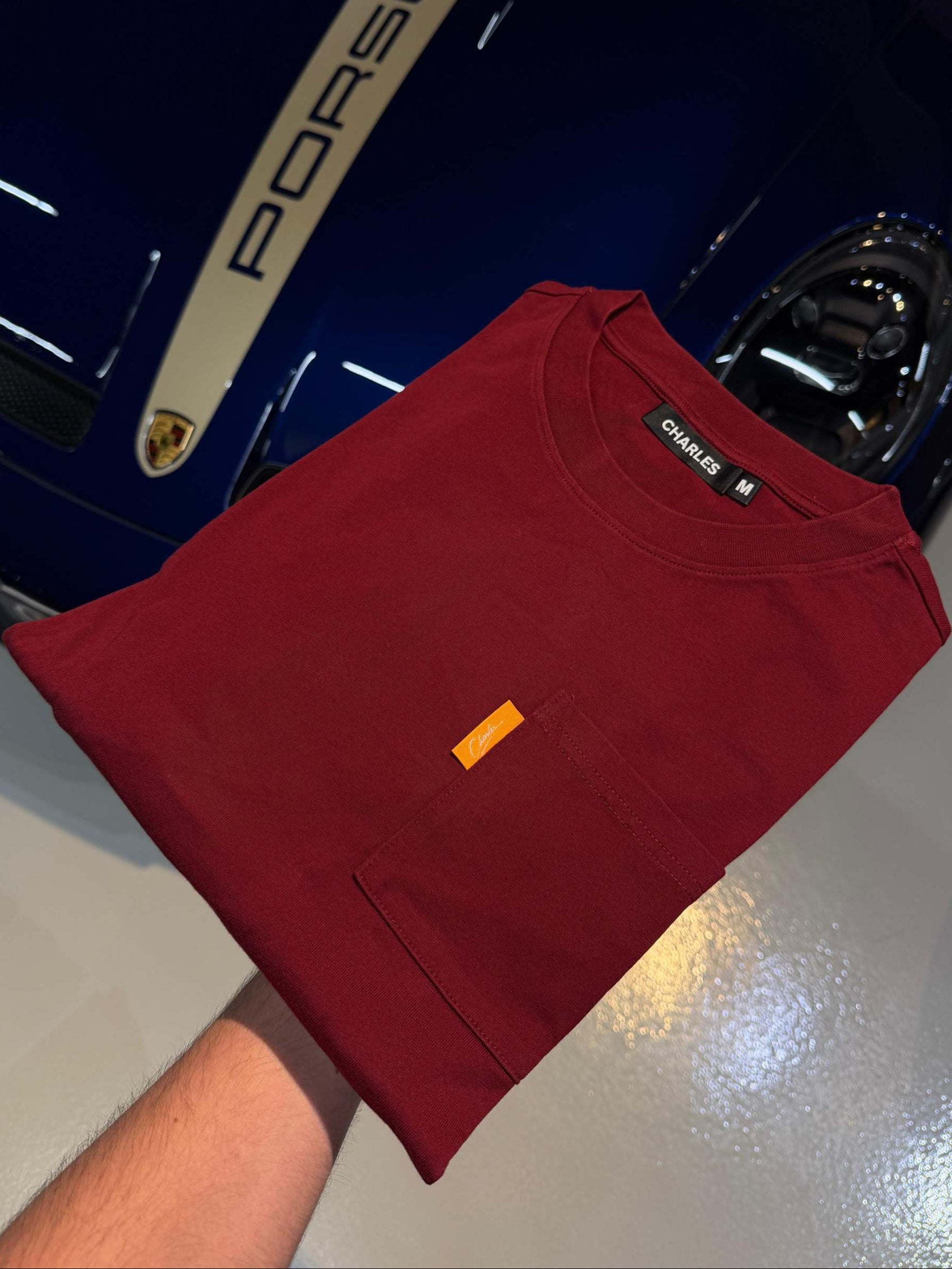 Studio By Charles burgundy long sleeve tee folded on blue Porsche car hood