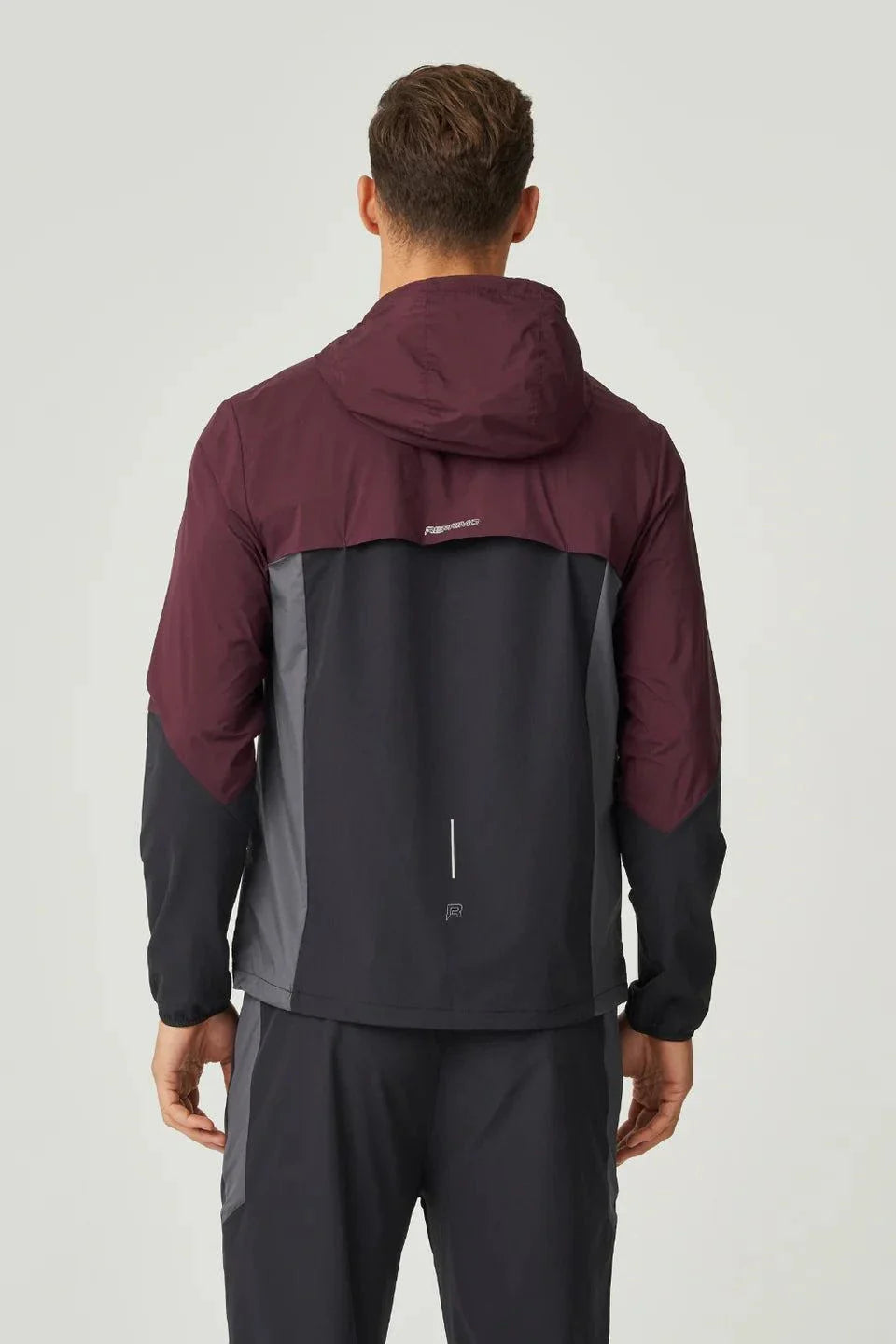 Back view of man wearing burgundy and obsidian Reprimo Impact Windbreaker with hood and dual-fabric construction.