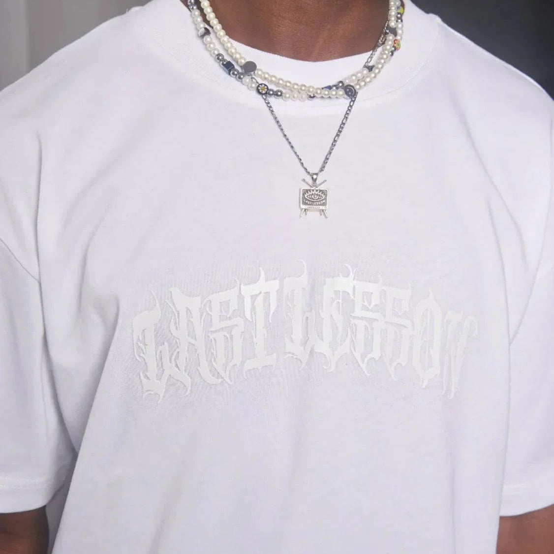 Last Lesson white puff print t-shirt on person with necklaces.