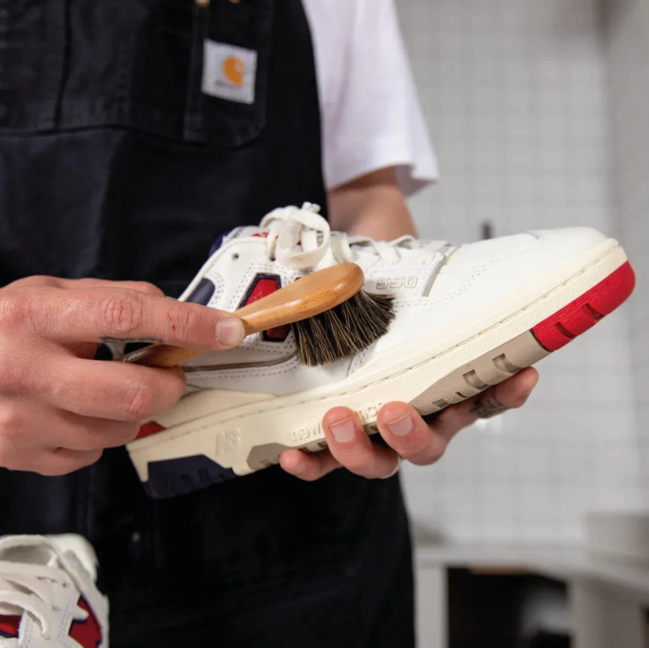 Person applying superhydrophobic sneaker protector with horsehair brush on white sneaker with red sole