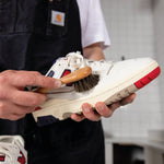 Person applying superhydrophobic sneaker protector with horsehair brush on white sneaker with red sole