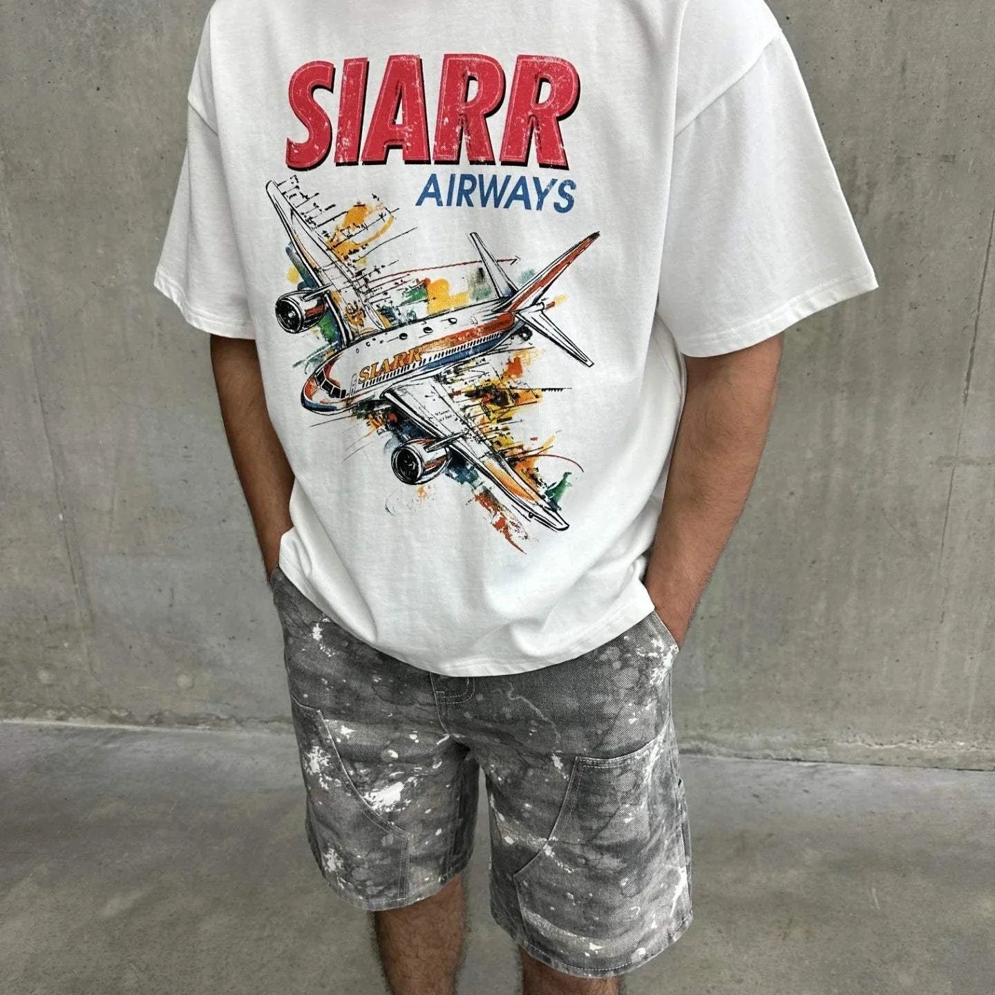 White oversized Siarr Aeroplane Tee with ribbed neck and colorful airplane screen print, worn with casual shorts.