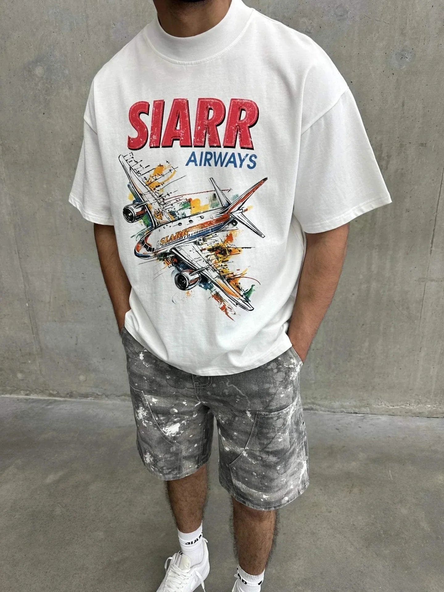 White oversized Siarr Aeroplane Tee with ribbed neck and colorful airplane screen print, worn with casual shorts.
