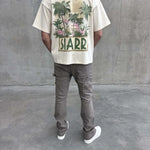 Back view of a person wearing a cream oversized Siarr Palm Tee with palm tree graphic and "SIARR" text, paired with grey pants and white shoes.